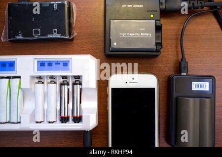Lots of charger devices as mobile, rechargable batteries, camera batteries, etc. Overhead shot.