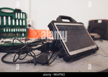 car mechanic maintains a vehicle with the help of a diagnostic computer - modern technology in the car repair shop Stock Photo