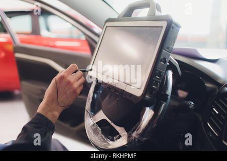 car mechanic maintains a vehicle with the help of a diagnostic computer - modern technology in the car repair shop Stock Photo