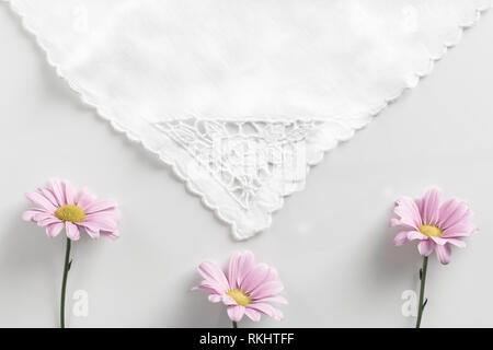 Flat lay of three pink daisy flowers, on a white background, laying under a triangular piece of cotton, creating an envelop style layout. Stock Photo