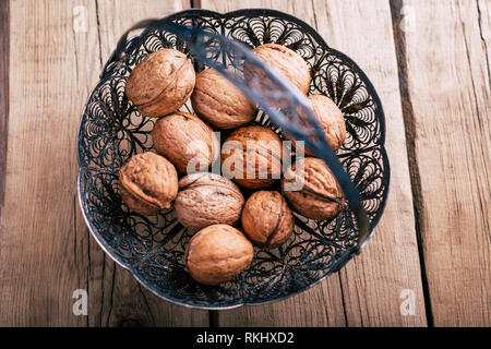 From above ornamental metal basket with fresh walnuts placed on wooden tabletop Stock Photo