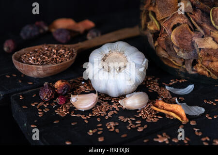 Garlic, dried fruit and seeds in dark rustic background. Artistic photo of garlic and dry fruit on old black table shot in low key ciaroscurro style Stock Photo