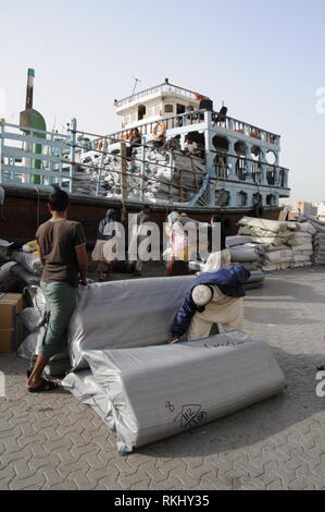 A group of Asian dock workers (dockers) preparing goods for export to be loaded onto a moored Dhow ( Arab boat on the quayside of the Dubai Creek in D Stock Photo