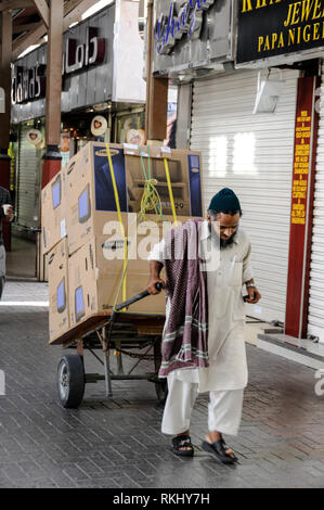 An Asian labourer pulling his cart making a delivery of Television sets to one of the small retailers in the Dubai Gold Souk located in the district o Stock Photo