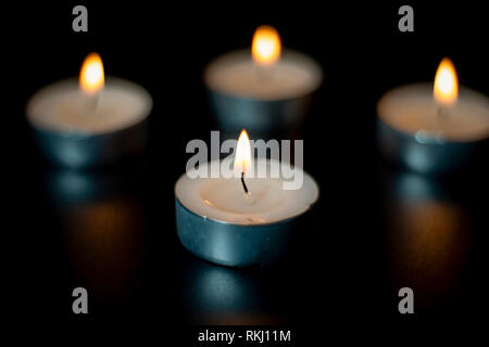Four tea candles with reflection on black background. Selective focus. Stock Photo