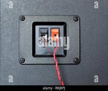 Red and black twisted wire connected to cable connection socket on rear side speaker system box front view closeup Stock Photo