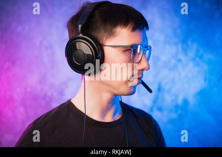 Gamer or streamer in earphones with microphone over colorful pink and blue neon lit wall Stock Photo