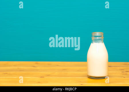 Fresh creamy milk in a one-third pint glass milk bottle, on a wooden table against a bright teal painted background Stock Photo