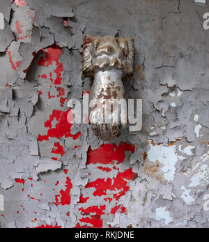 Rusty hand shaped door knocker on a silver colored door with paint peeling off revealing prior red point. Focus on the knocker. Stock Photo