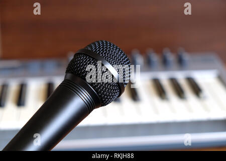 Black vocal microphone close up against defocus electronic synthesizer keyboard with many control knobs in silver plastic body as background Stock Photo