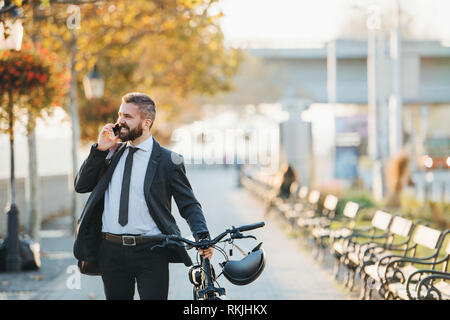Businessman commuter with bicycle walking home from work in city, using smartphone. Stock Photo