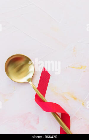 Golden spoon in red ribbon on a pink background . Spring holidays cooking and celebration concept. Top view, flat lay, copy space. Stock Photo