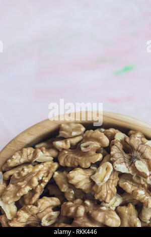 Walnuts kernels, peeled nuts in a wooden bowl on a pink background, concept of healthy eating vegan food Close up, selective focus. Stock Photo