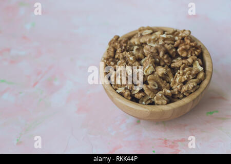 Walnuts kernels, peeled nuts in a wooden bowl on a pink background, concept of healthy eating vegan food Close up, selective focus. Stock Photo