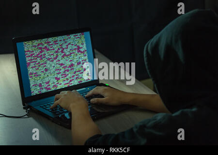 Dangerous hooded hacker on laptop breaks internet code and spread virus on a computer systems Stock Photo