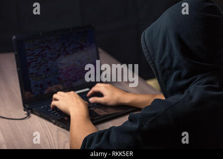 Dangerous hooded hacker on laptop breaks internet code and spread virus on a computer systems Stock Photo