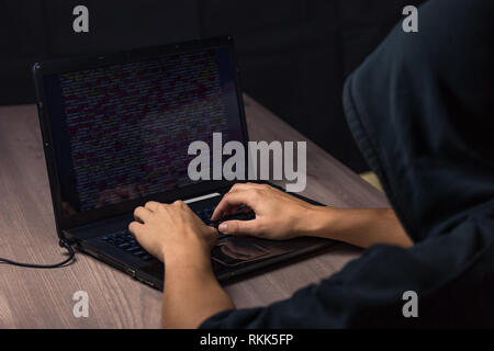 Dangerous hooded hacker on laptop breaks internet code and spread virus on a computer systems Stock Photo