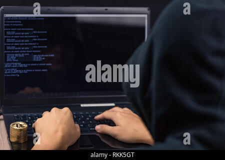 Dangerous hooded hacker on laptop breaks computer security sistem and steal bitcoin cryptocurrency Stock Photo