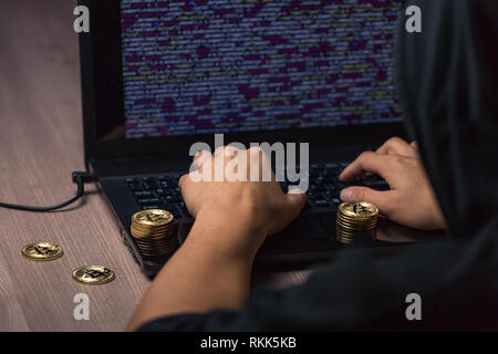 Dangerous hooded hacker on laptop breaks computer security sistem and steal bitcoin cryptocurrency Stock Photo
