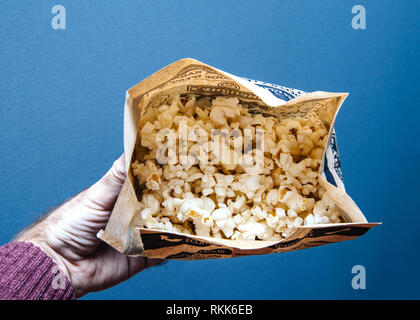Man hand holding bag of popcorn against blue background - ready for the new blockbuster cinema movie Stock Photo