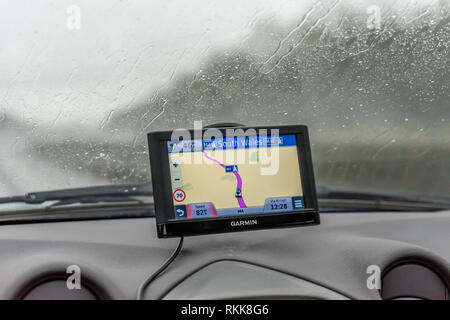 A Garmin sat nav or satellite navigation / satnav system mounted to a car wind screen during rainy weather driving in Wales, UK, Europe Stock Photo