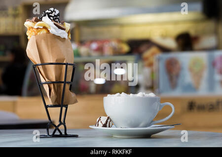 Ice cream dessert in wafer cup with chocolate cookies and and mug of coffee with marshmallows on porcelain plate on blurred colorful copy space backgr Stock Photo