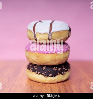 Stack of sweet glazed doughnuts on pink background. Stock Photo