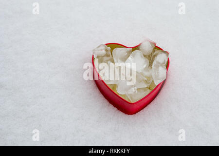 Minimalist setup with a red, heart shaped box, on a snow background. Abstract concept for 14 February. Stock Photo