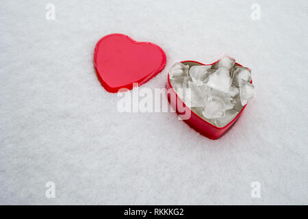 Saint Valentine's Day concept with a red box in form of a heart, with ice cubes inside it and the red lid set on the side, on top of a snow layer back Stock Photo