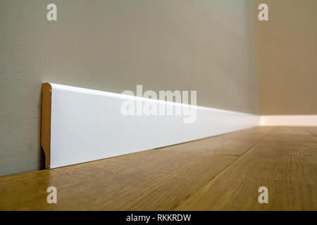 Wooden or plastic white floor plinth installation in big empty room on wooden floor and white plastered stucco walls background. Interior details. Stock Photo