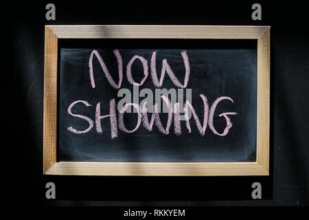 Now showing - words hand written with chalk on blackboard Stock Photo