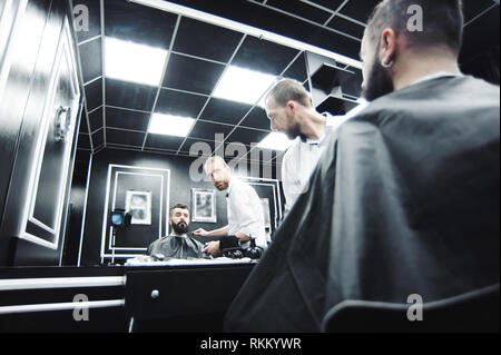 Master cuts hair and beard of men in the barbershop, hairdresser Stock Photo