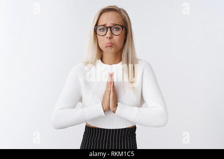 Whining girl in glasses with blond hair holding hands in pray pouting frowning making silly sad face begging apology praying saying sorry, need advice Stock Photo