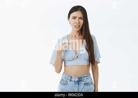 Woman feeling confused being blamed or chosen. Portrait of displeased bothered and questioned asian girlfriend frowning pointing at chest with finger Stock Photo