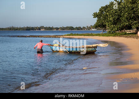 Cuban fisherman is pulling out his old blue boat with furled sails in the morning from the sandy beach in hope to catch some fish. Cuba Stock Photo