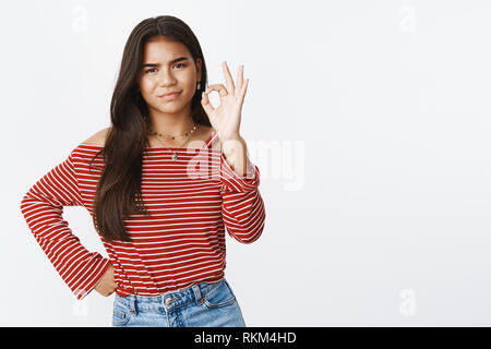 Fine I cannot say no. Portrait of intense bothered and displeased young indian teenage girl smirking from dislike as showing okay sign as approving Stock Photo