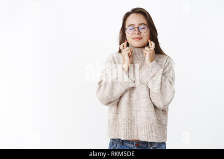 Portrait of charming dreamy girl making wish with crossed fingers for good luck and closed eyes smiling optimistic having hope dream come true Stock Photo