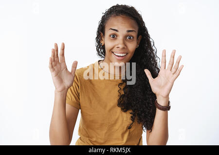 Amazed and thrilled happy young african-american woman with pretty dark curly hair gesturing with raised palms as describing exciting news smiling Stock Photo