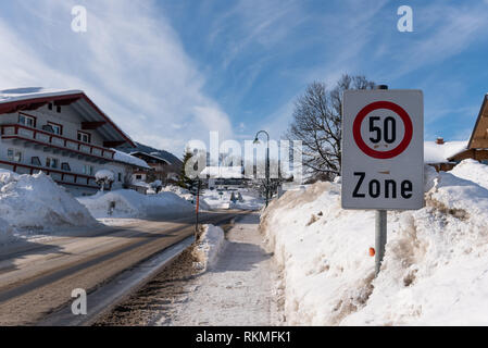 Traffic sign at built-up area. Speed zone 50 warning. Snow-covered road and snowdrifts on the pavement. Winter services, Schladming, Austria, Europe Stock Photo