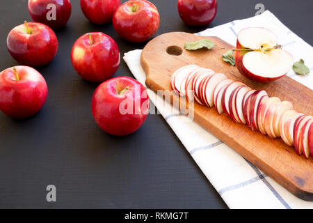 Slices of red apples on rustic wooden board on dark surface, side view. Stock Photo
