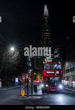 London street at night with Shard on background and red bus in front waiting for green light. Stock Photo