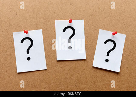 Three question marks pinned in a row with colorful red thumb tacks on a wooden notice board with copy space in a conceptual image Stock Photo