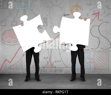 Two men assembling puzzles with business doodles on concrete wall Stock Photo