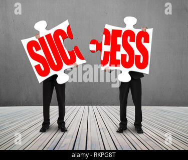 Businessmen standing and holding two puzzles with SUCCESS on wooden floor Stock Photo