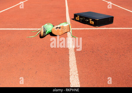 A black briefcase and a pair of broken green running shoes on a running track symbolizing competition, challenge and burnout in work and business. Stock Photo