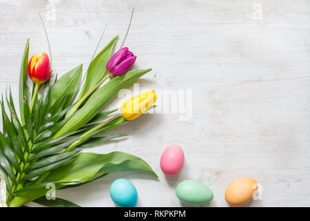 Easter colorful spring tulips with palm cross cake and eggs decoration on white wooden natural background Stock Photo