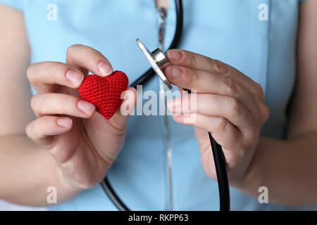 Woman doctor with stethoscope and red knitted heart in hand. Concept of cardiologist, heart diseases, diagnosis, auscultation, medical exam Stock Photo