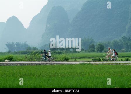 Tourists ride along a rural road surrounded by spectacular scenery in Yangshuo. Speckled with karst mountains and the gently flowing rivers, this regi Stock Photo