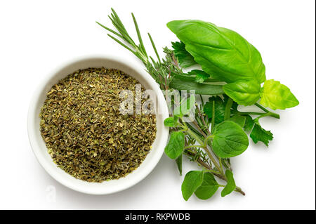 Dried chopped provence herbs in a white ceramic bowl next to fresh bouquet garni isolated on white from above. Stock Photo