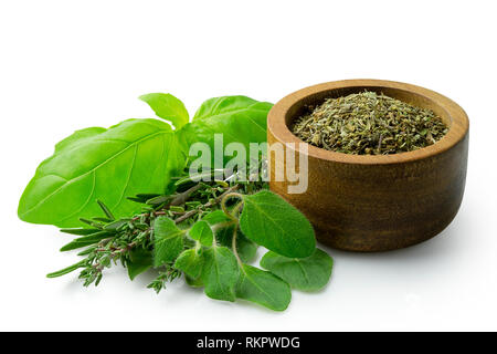 Dried chopped provence herbs in a dark wood bowl next to fresh bouquet garni isolated on white. Stock Photo